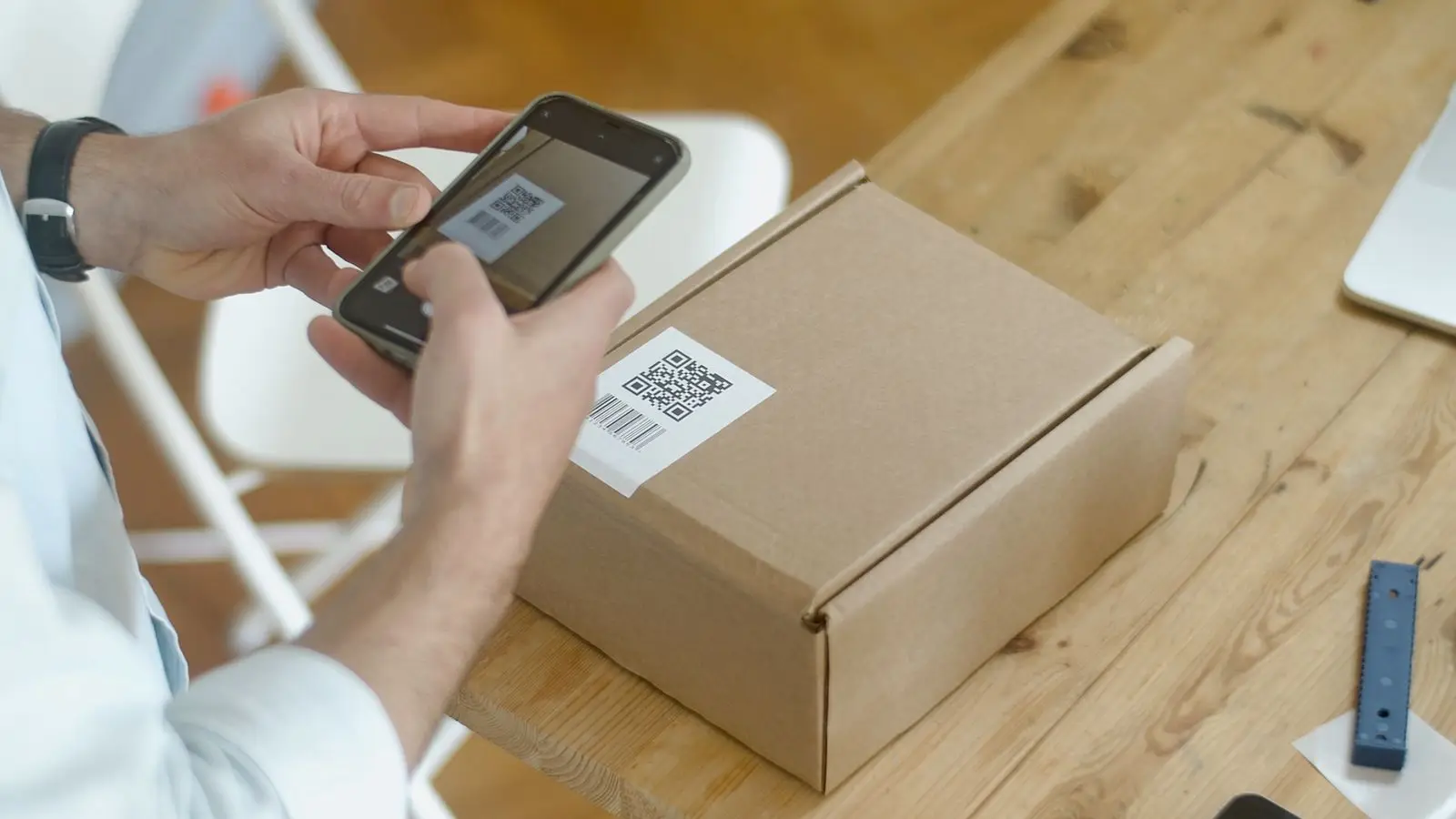 Hands scanning the barcode label on a cardboard box with a smartphone camera