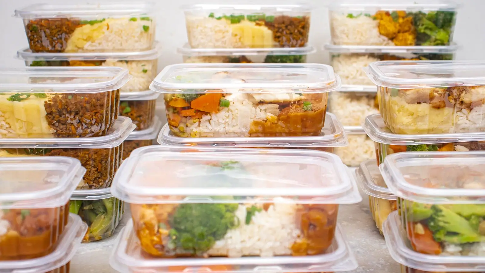 Stacks of lidded containers filled with batch-cooked rice, meat and vegetable meals