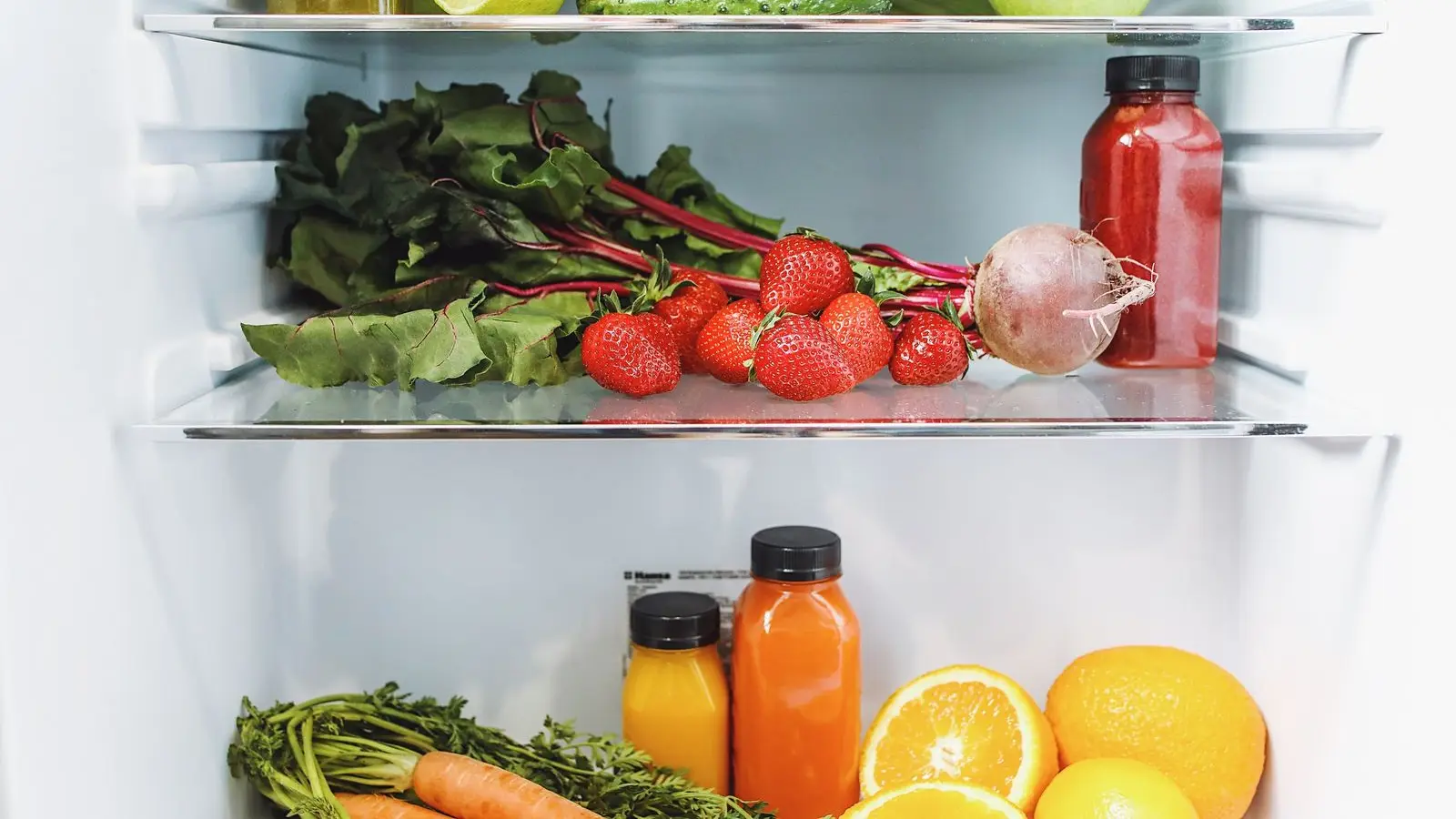Fridge shelves holding strawberries, beets, celery, citrus, carrots and bottled juices