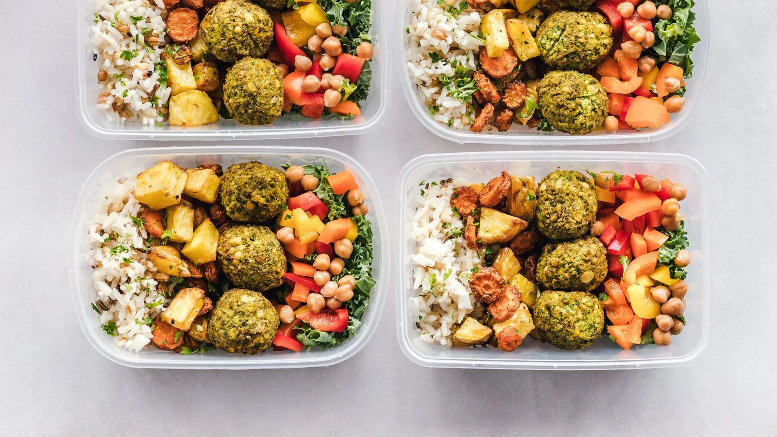 Four meal prep containers of rice, roasted vegetables, falafel and chickpeas