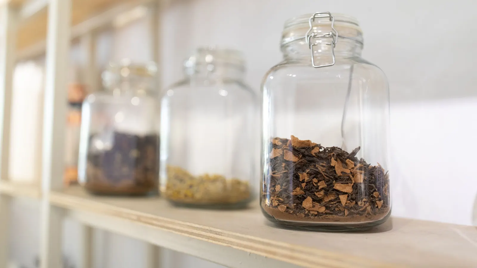 Glass jars of dried food lined up on a plain wooden storage shelf