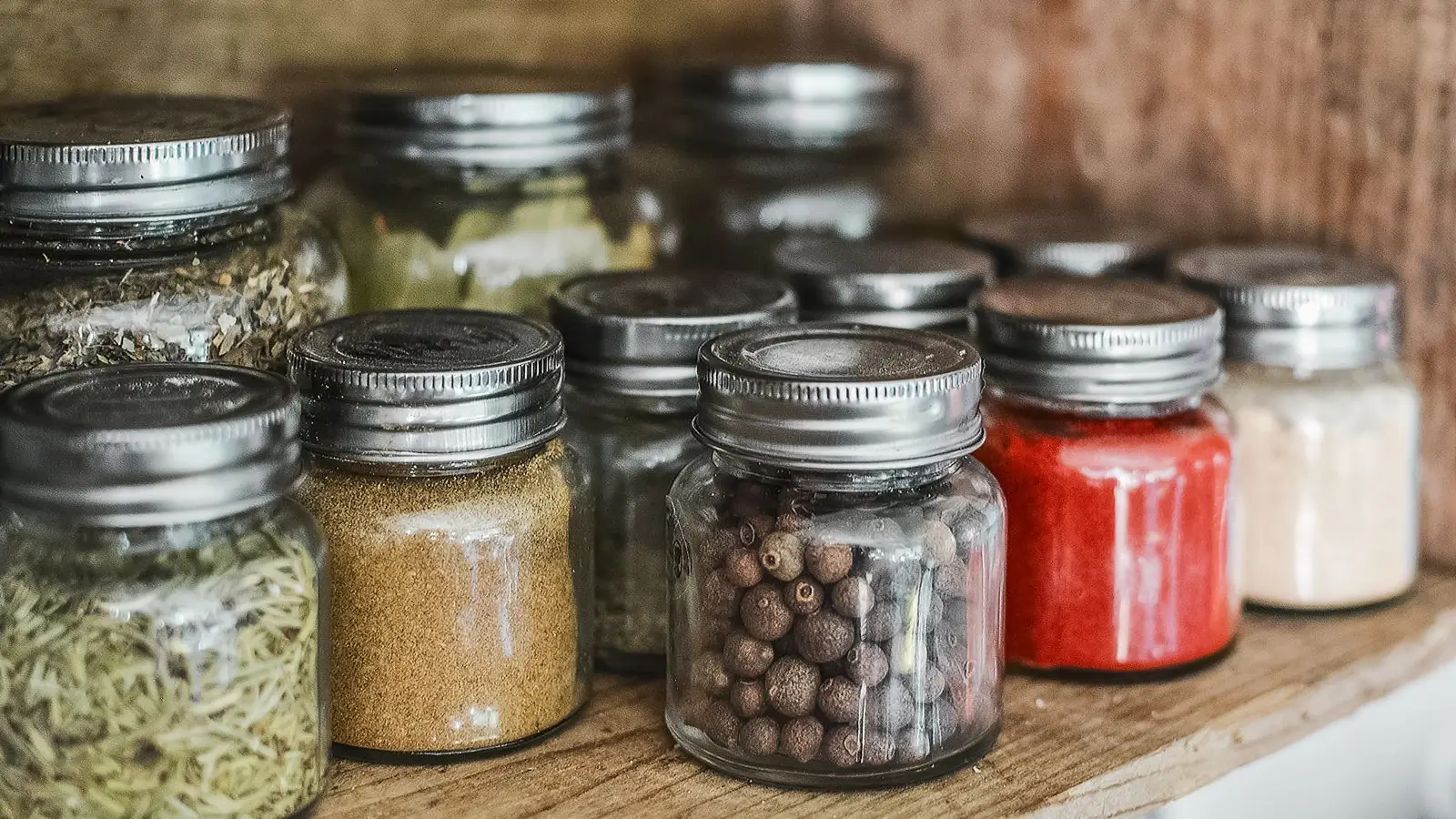Small glass spice jars with metal lids on a wooden shelf