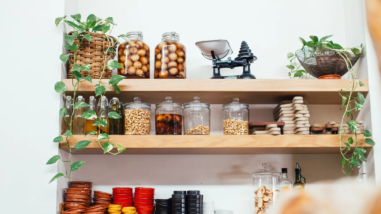 Open wooden pantry shelves with glass jars of nuts and preserves, oils, and stacked bowls