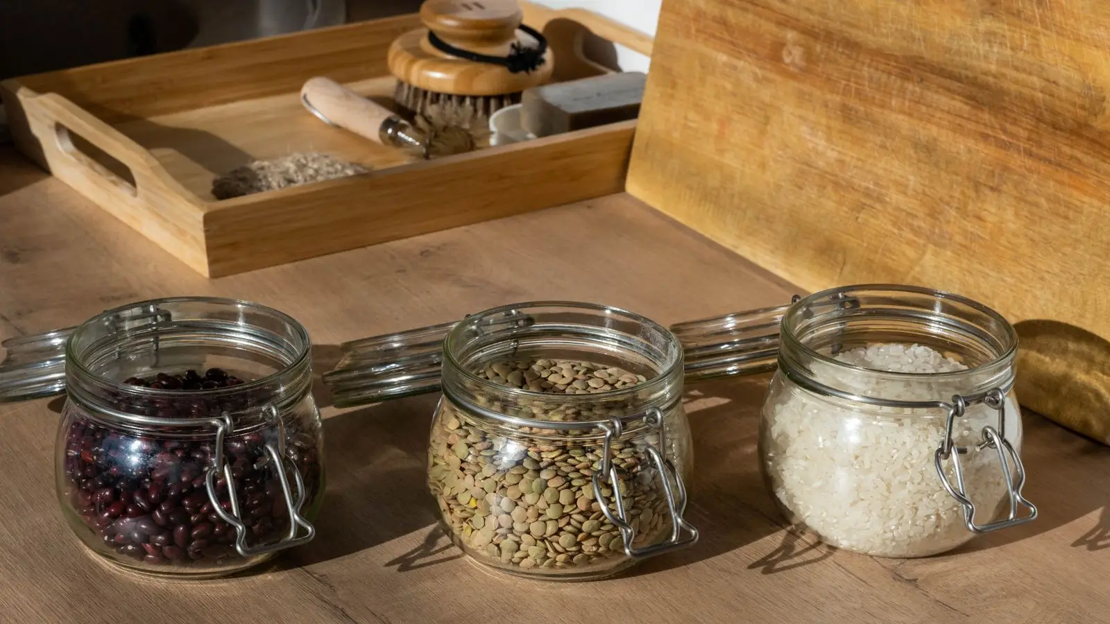 Three glass jars of dried beans, lentils and rice on a wooden counter