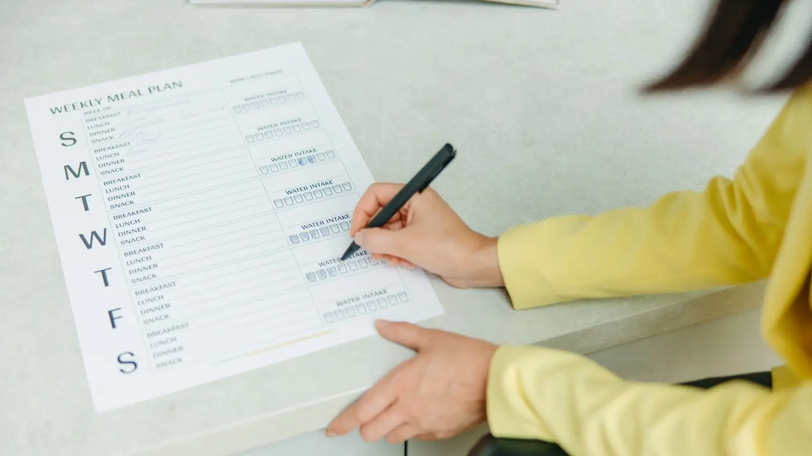 Hand filling in a printed weekly meal plan sheet on a kitchen counter