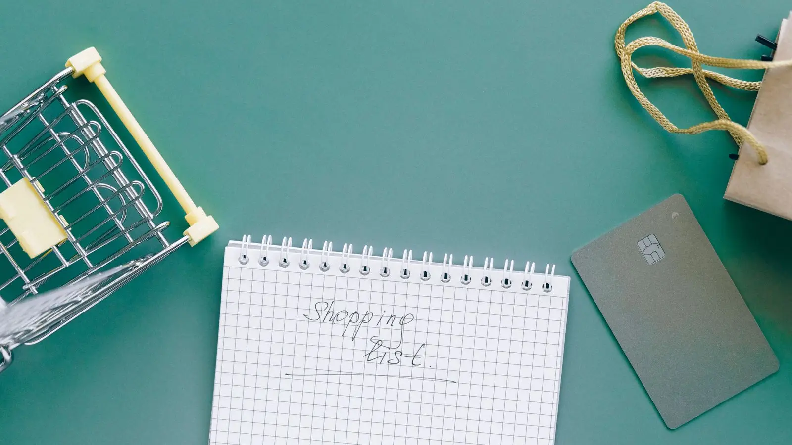 Notepad headed "Shopping list" beside a toy shopping cart, bank card and paper bag