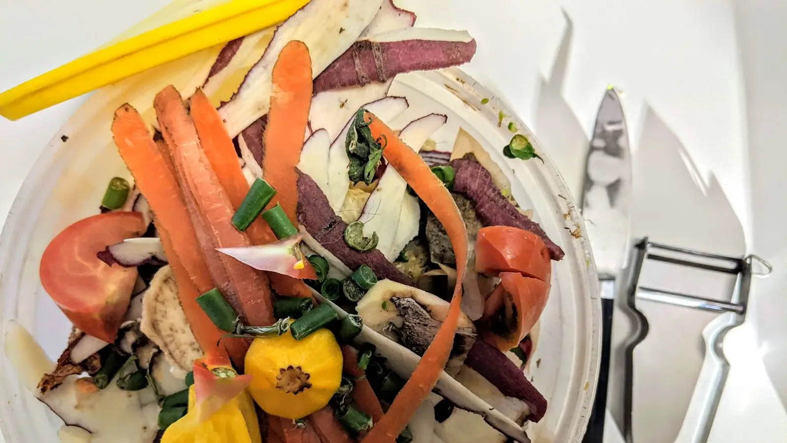 Bowl of vegetable peels and scraps next to a knife and peeler