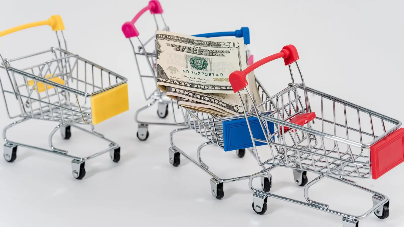 Miniature shopping carts, one holding folded dollar bills