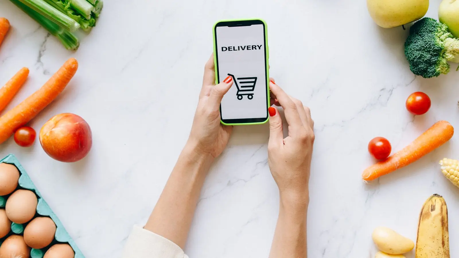 Hands holding a phone showing a shopping cart icon, surrounded by fresh produce and eggs