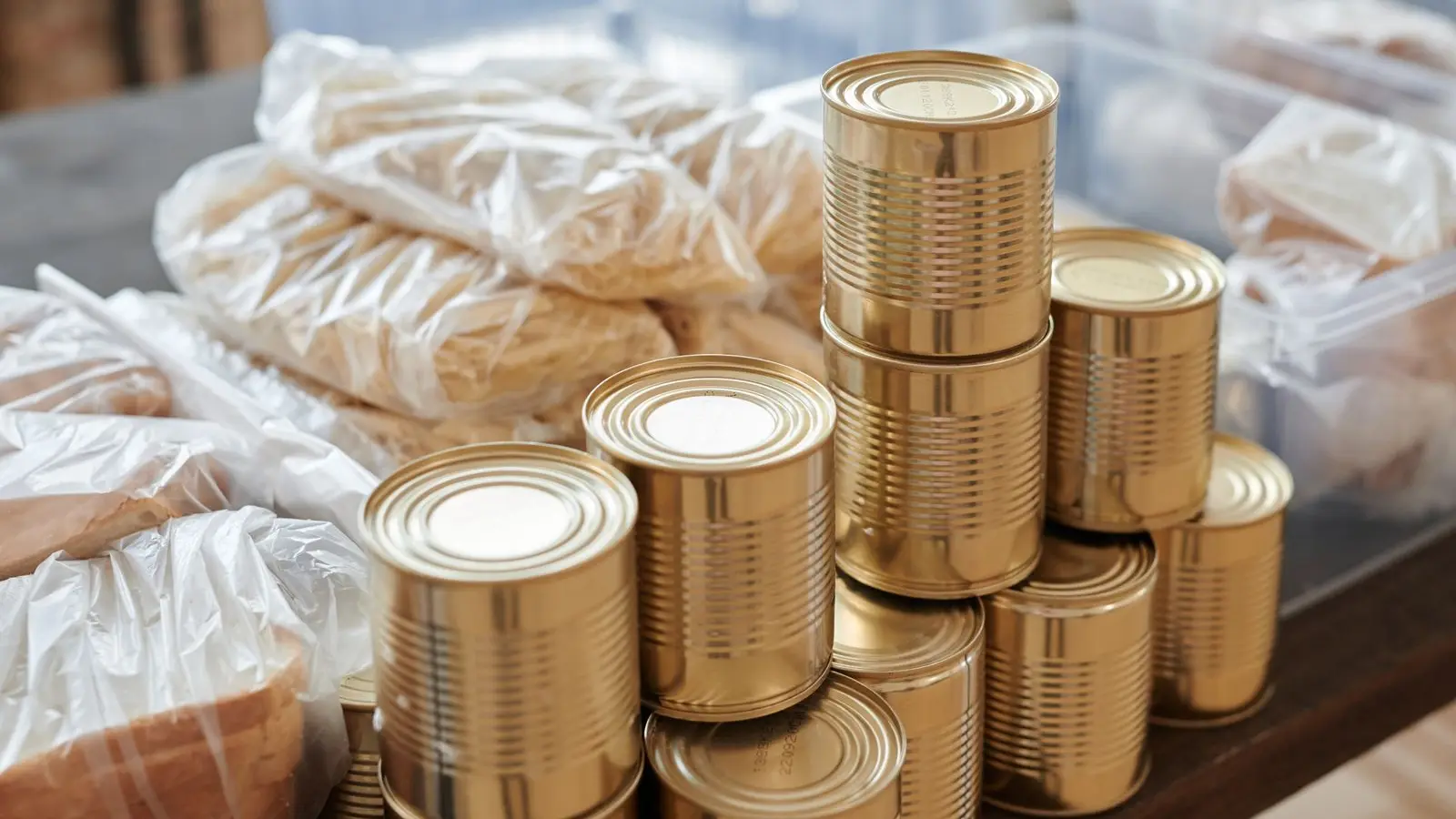 Stacks of identical unlabeled cans beside bags of dry pasta and bread