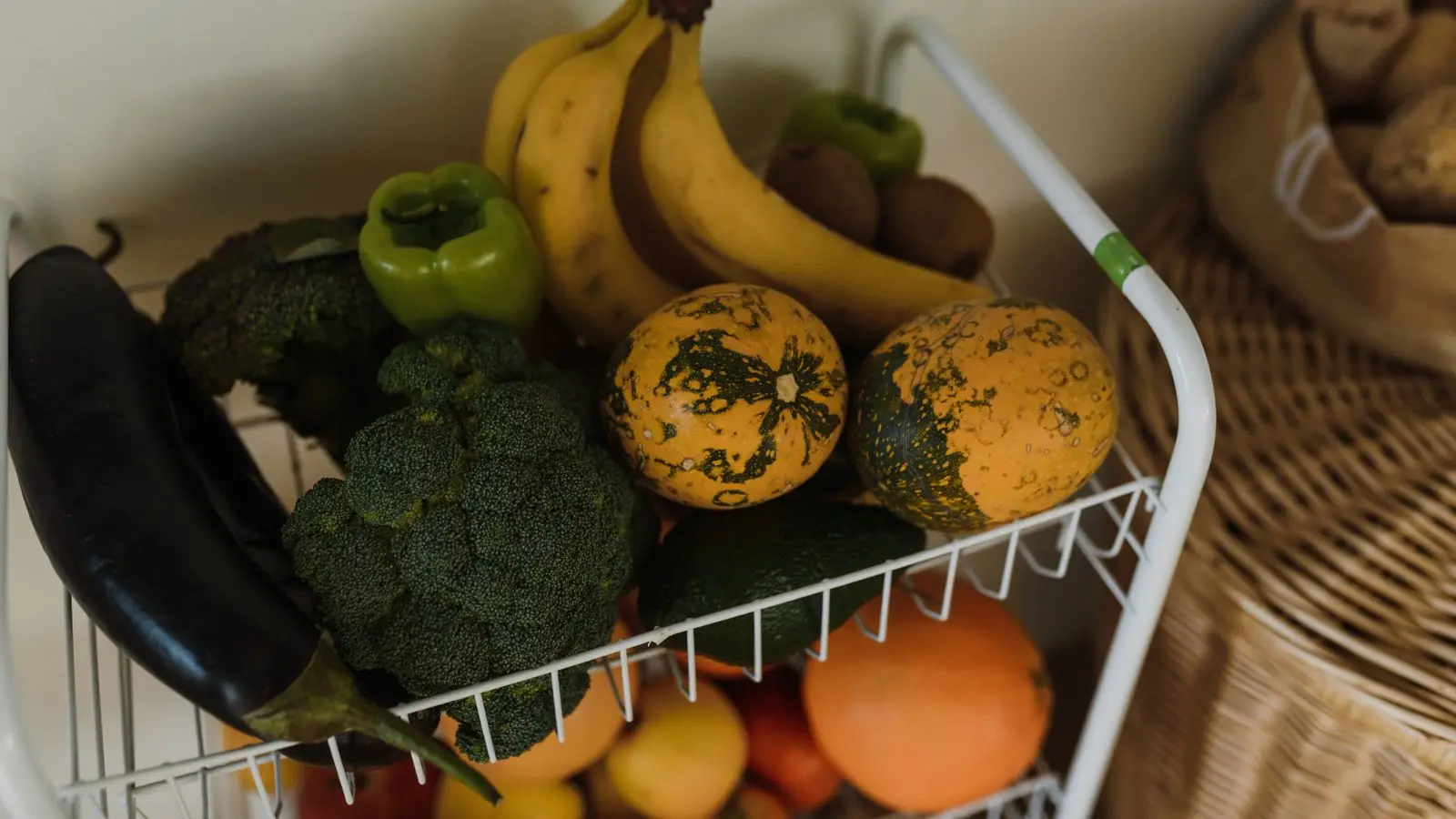 Wire produce rack holding bananas, broccoli, squash, peppers, eggplant and oranges