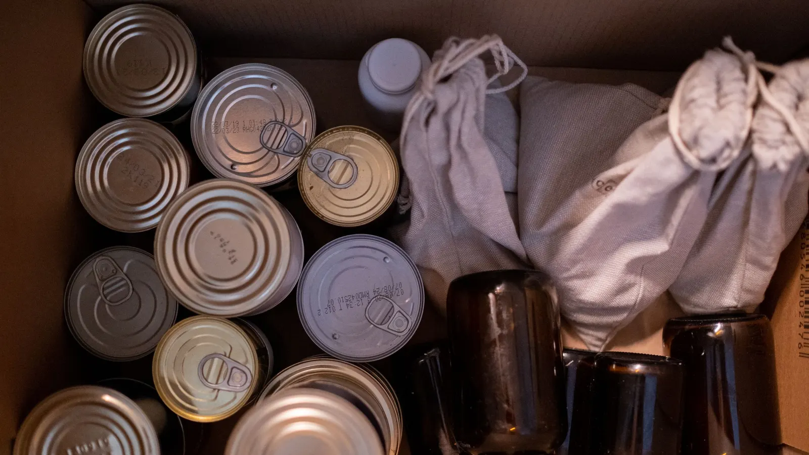 Top view of a cardboard box packed with canned goods, glass jars and cloth sacks