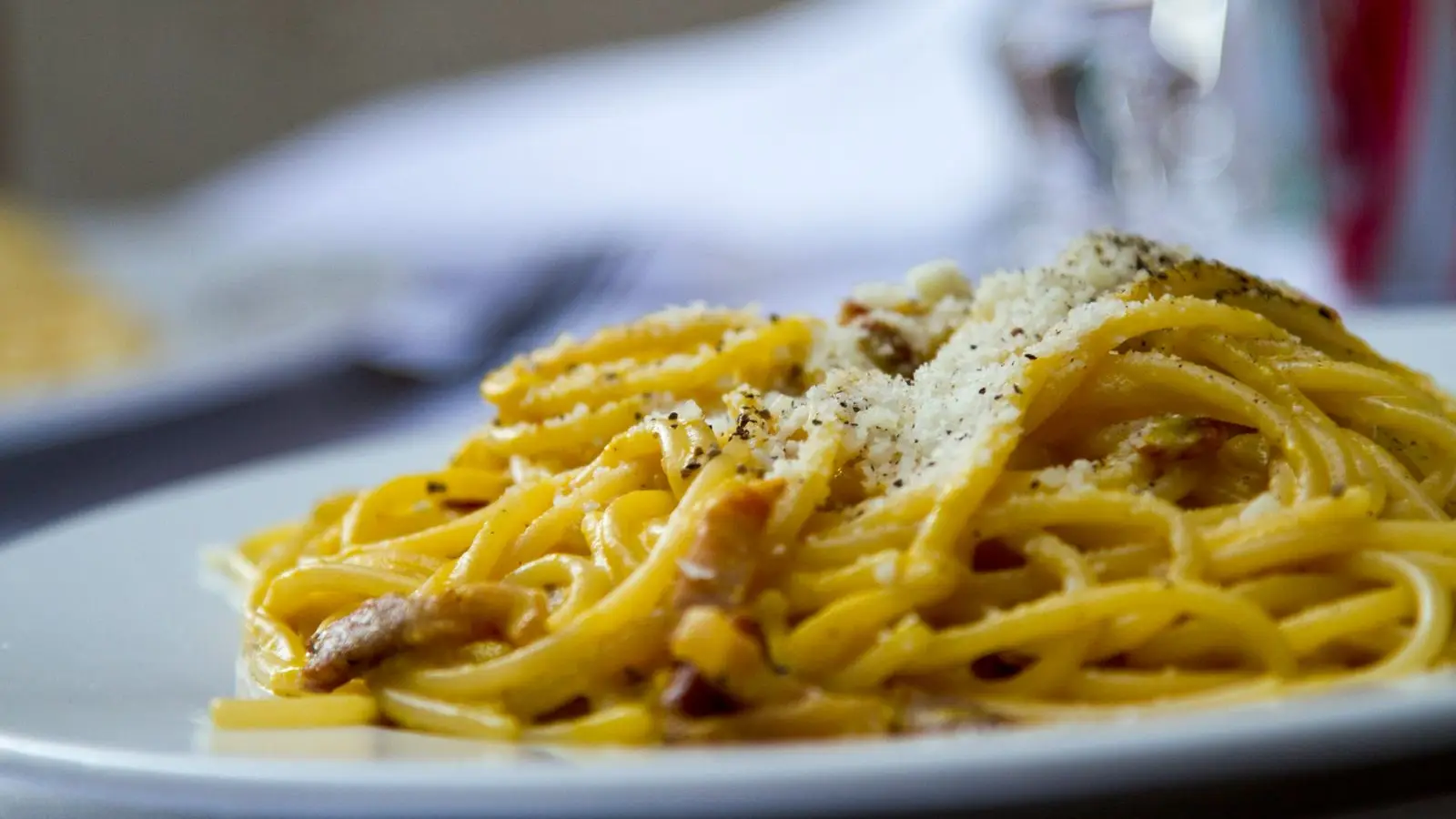 Plate of spaghetti carbonara topped with grated cheese and black pepper